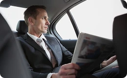 Businessman in a suit reads a newspaper while relaxing in a premium backseat—capturing luxury, quiet, and comfort during travel.