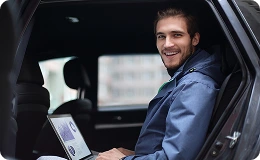 Smiling man with a laptop enjoys a relaxed ride in the backseat, ready for a customized travel experience with flexible stops.