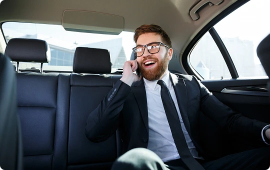 Smiling businessman in a suit enjoys a lively phone conversation while riding in the backseat of a luxury car—blending comfort, connection, and executive travel with ease.