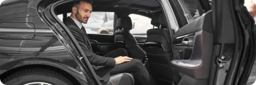 Chauffeur opens the door of a luxury black car for a passenger, reflecting premium, direct travel experience.