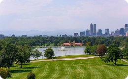 Expansive view of Washington Park with lush green lawns, a serene lake, and Denver's skyline in the background—perfect blend of nature, recreation, and urban charm.