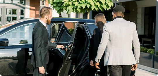 Chauffeur opens the door of a sleek black SUV as two well-dressed passengers approach—capturing a moment of polished service, elegance, and professional travel ambiance.