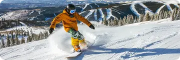 Snowboarder carves down a sunlit slope at Breckenridge Ski Resort, surrounded by pine-covered mountains and fresh powder.