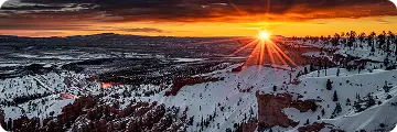 Vibrant sunset over snowy hills and pine trees in Beaver Creek Village, casting warm light across a dramatic winter landscape.