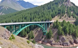 Scenic view of Red Cliff's green steel bridge spanning a rocky gorge, surrounded by dense pine forest and mountainous terrain.