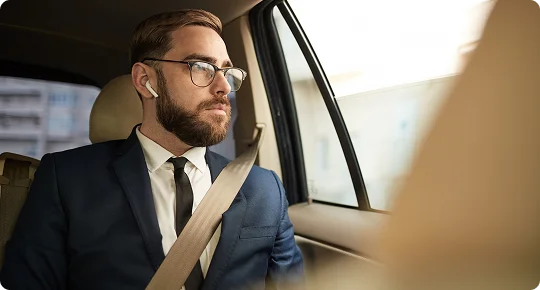 Bearded businessman in a suit wearing wireless earbuds looks out the window while seated in the backseat of a luxury vehicle—capturing a calm, focused moment during an executive car service ride.