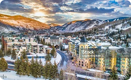 Scenic winter view of Vail Village with colorful alpine buildings, snowy mountains, and a dramatic sunset sky—capturing the charm of a luxury ski destination.
